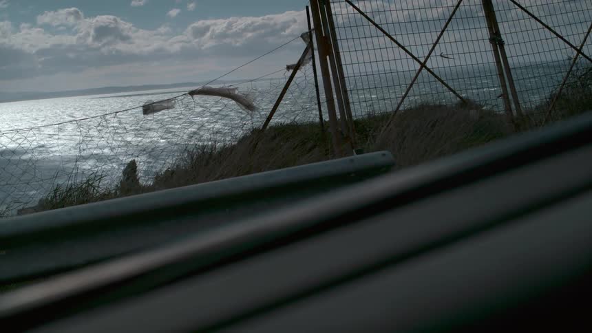 The ocean seen from behind an old fence and a highway barrier