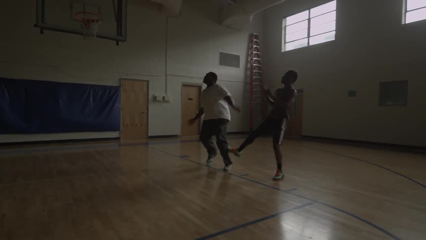 Two men are playing basketball on a court indoors during the day