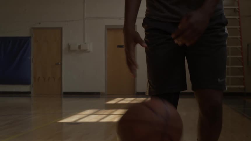 A man is dribbling a basketball on a court inside during the day