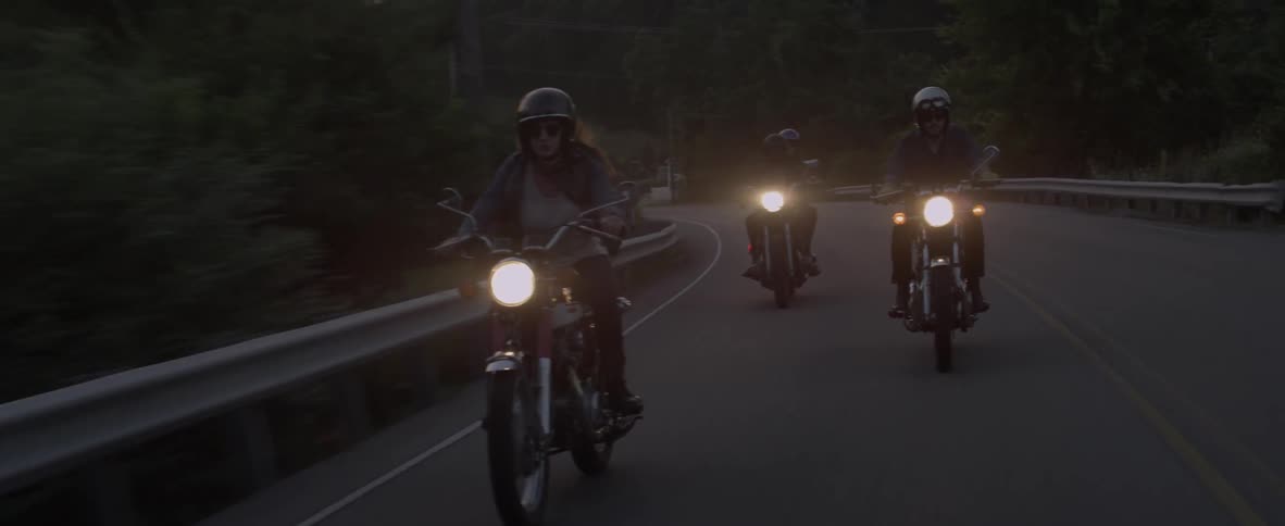 A woman and her friends ride motorcycles on a rural road at dusk
