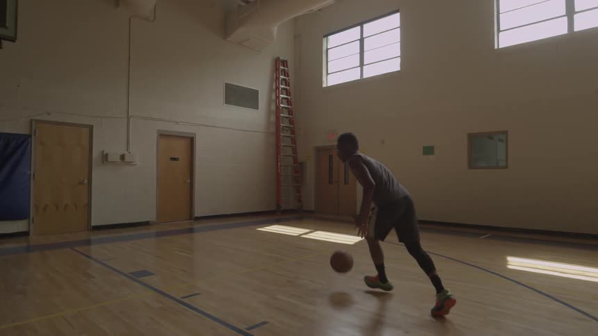 A man is sinking a basketball shot on a court inside during the day