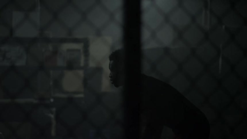 A man tosses and catches a ball in a dimly lit room