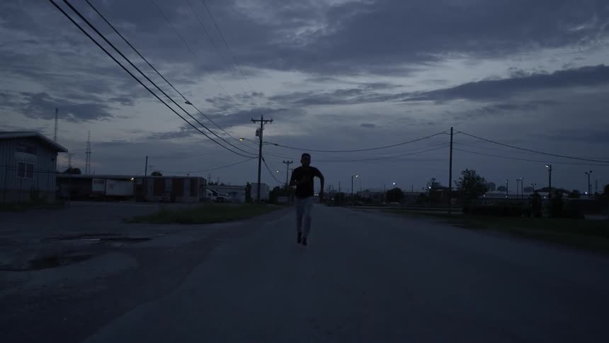 A man is running on a road at dusk under cloudy skies
