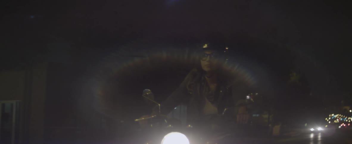 A woman rides a motorcycle at night