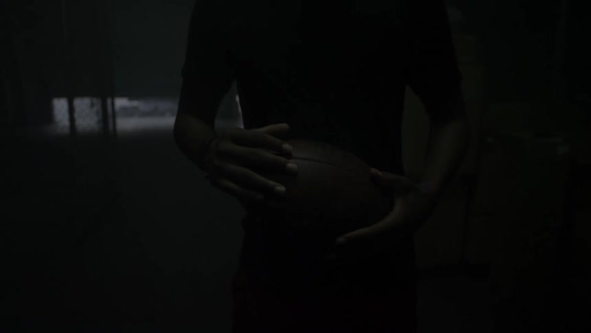 A man holds a football in a dimly lit room