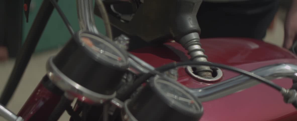 A woman is filling her motorcycle's tank with fuel