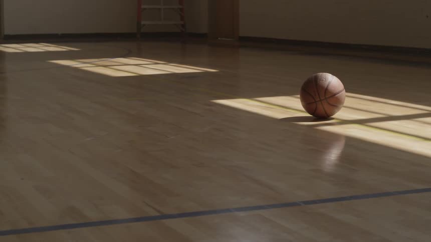 A basketball sits idle on a hardwood floor during the day