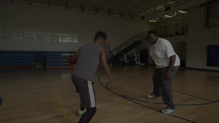 Two men are playing basketball on a court indoors during the day