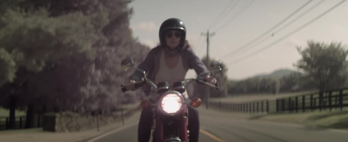 A woman is riding a motorcycle on a rural road