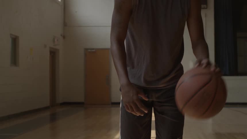 A basketball player is bouncing a ball on a court inside during the day