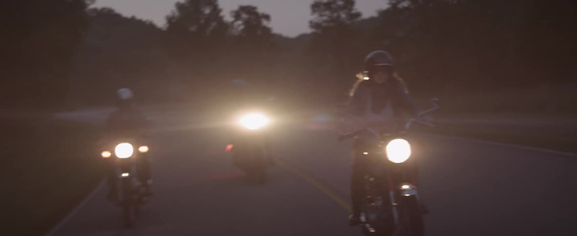 A group of motorcyclists drive at dusk