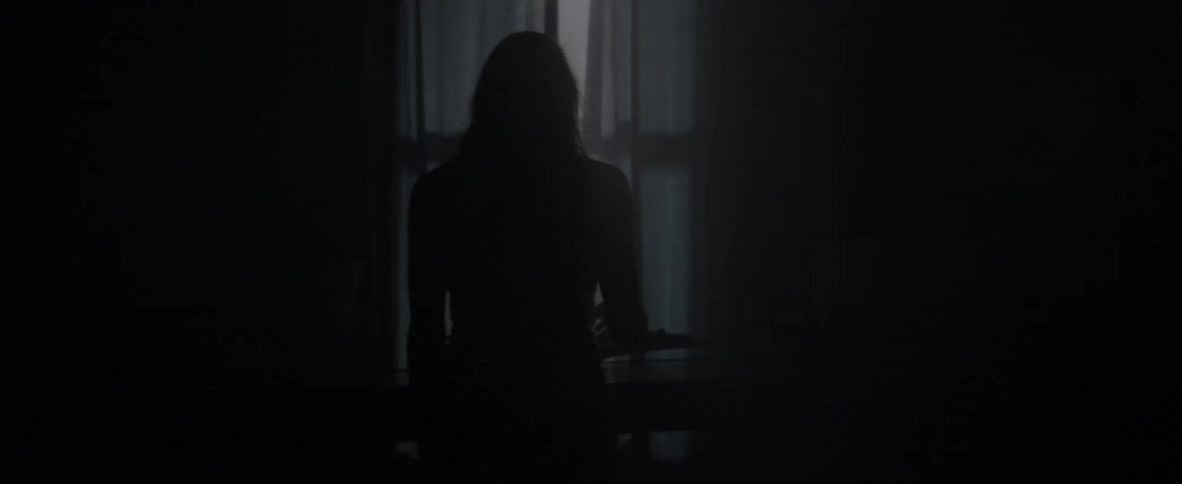 A woman walks to an open window with curtains