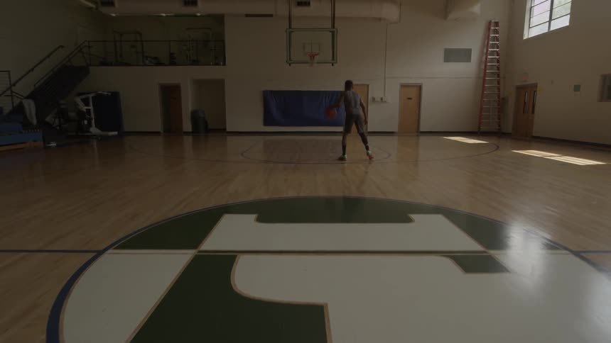 A man dribbles a basketball in an empty court