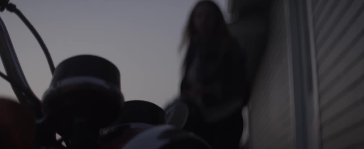 A woman exits a building and gets on a motorcycle at dusk