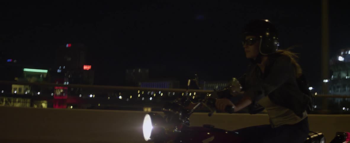 A woman rides on a motorcycle at night