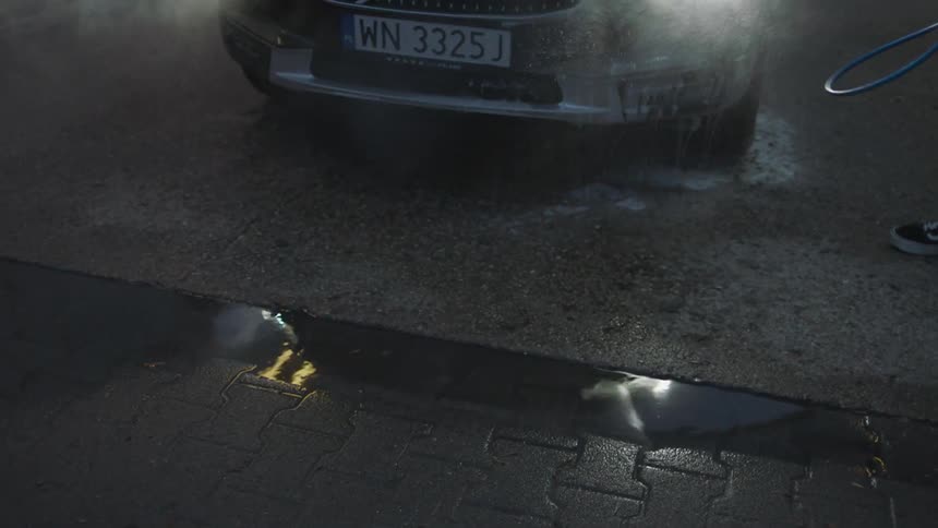 A man is washing a vehicle in a carwash at dusk
