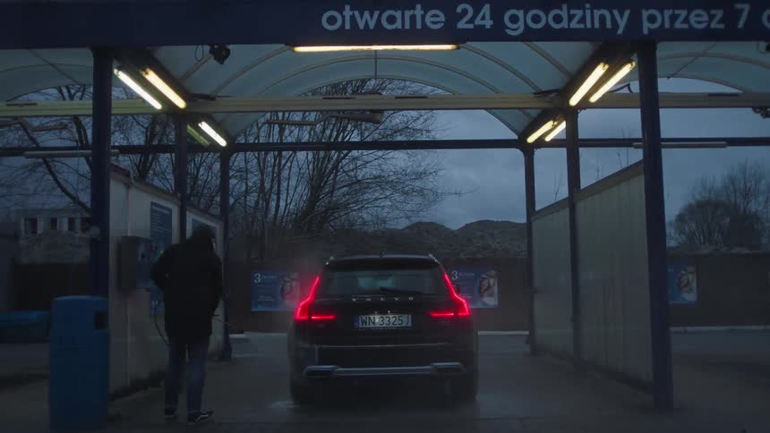 A man is washing a vehicle in a carwash at dusk
