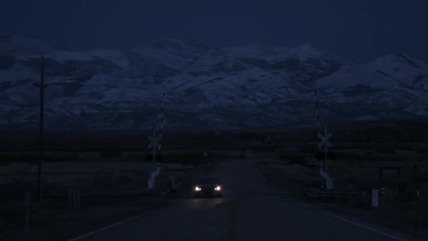 Car drives on a rural road with snowy mountains in the distance