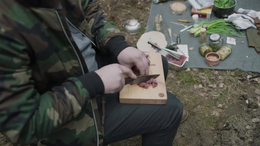 A man cuts meat outside on a cutting board