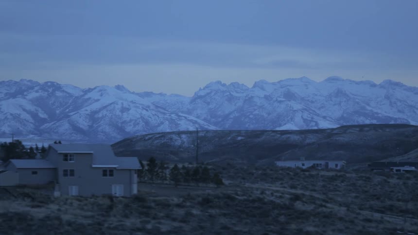 Snow covered mountains sit on the horizon behind homes in a rural area