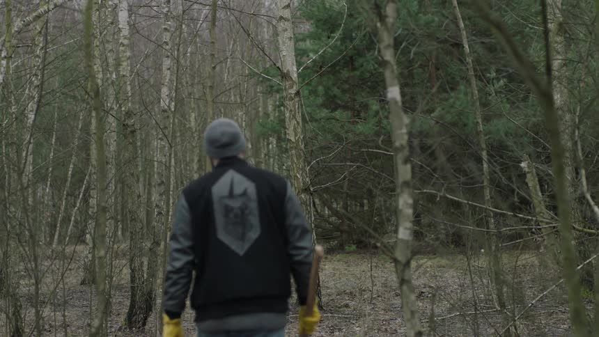 A man hikes through the woods carrying an ax