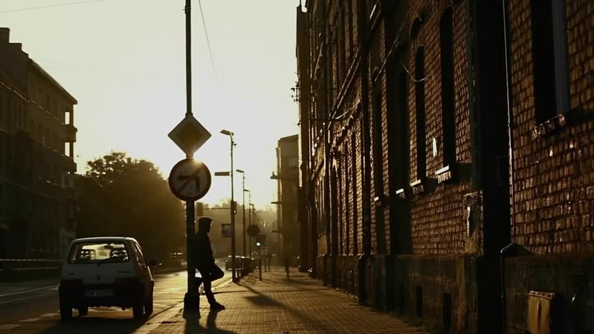 Man leaning against a post on a sidewalk smoking