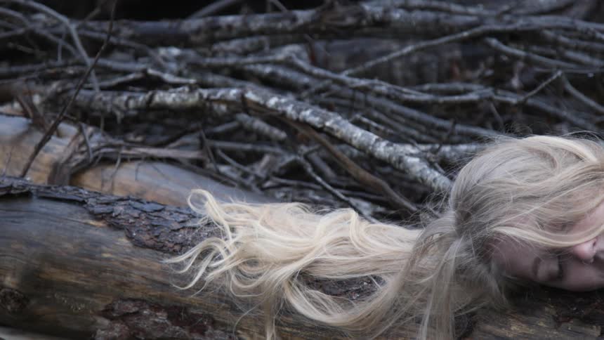 A woman lays motionless on a fallen tree