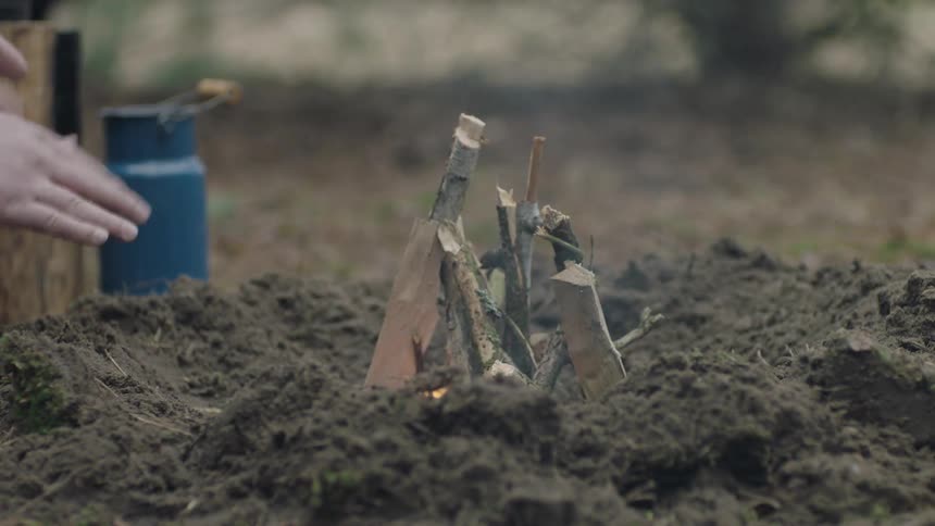 A man is building a campfire in the dirt