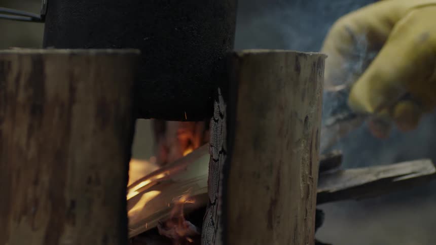 A person is putting kindling into a campfire being used as a stove