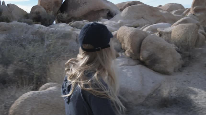 A woman is walking in a desert landscape covered in boulders