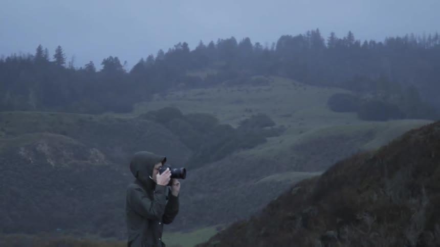A woman is taking pictures of a natural landscape on a cold day