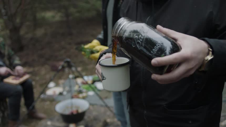 A man is pouring coffee from a ball jar into a camping cup
