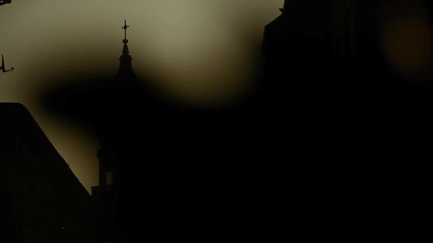 Sun glaring from behind the silhouette of a church steeple located in an urban area