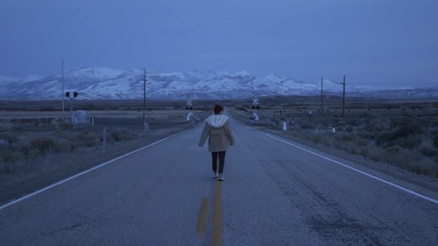 A woman wearing a jacket walks down the middle of a road