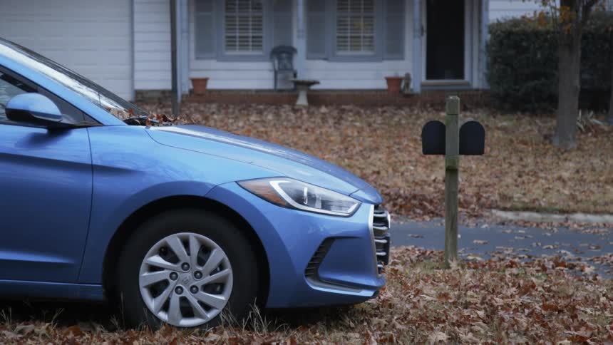 A blue car is parked outside of a house