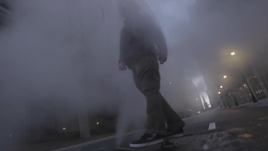 Man skateboards down foggy city street