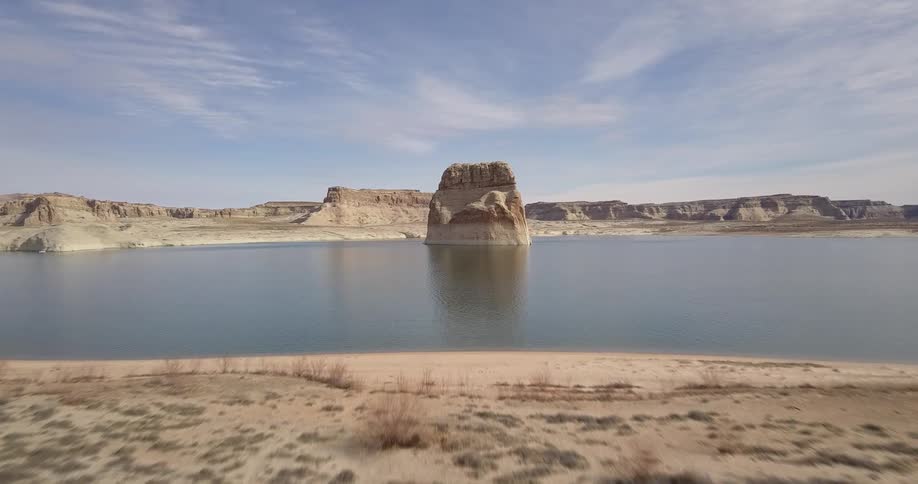 Large rock sits in a calm lake under a blue sky