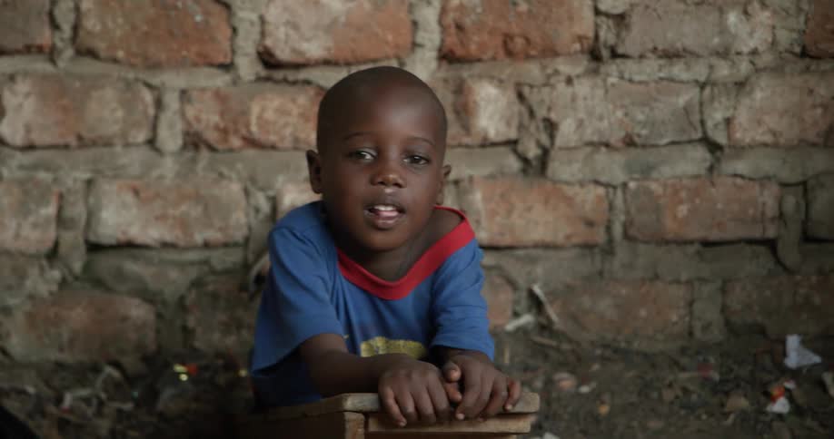 Young child on his tummy in front of a brick wall as he leans on a wooden block
