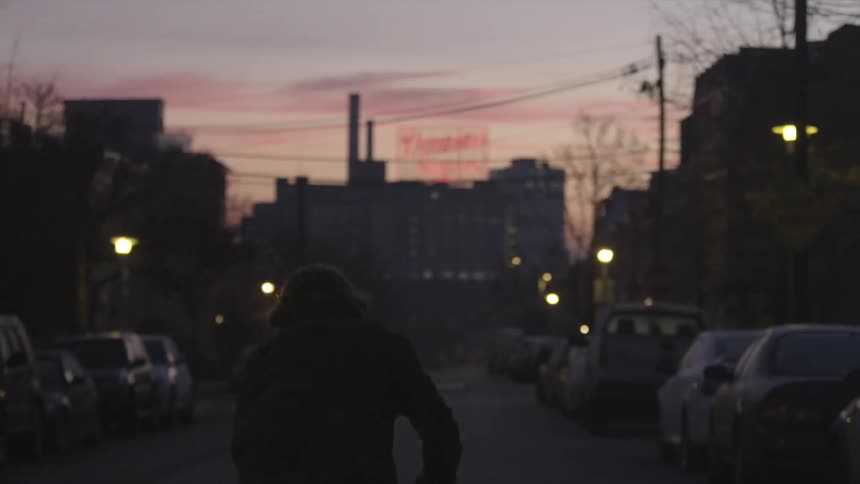 A skateboarder skates down the street at dusk