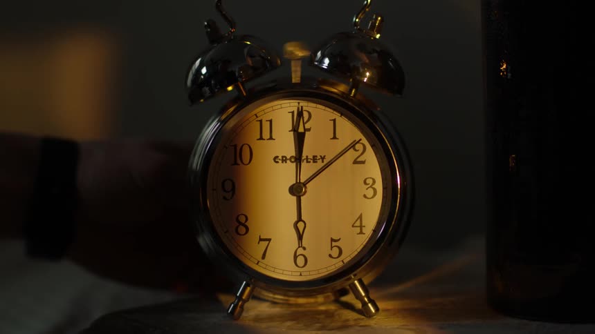 A hand turns off a ringing alarm clock