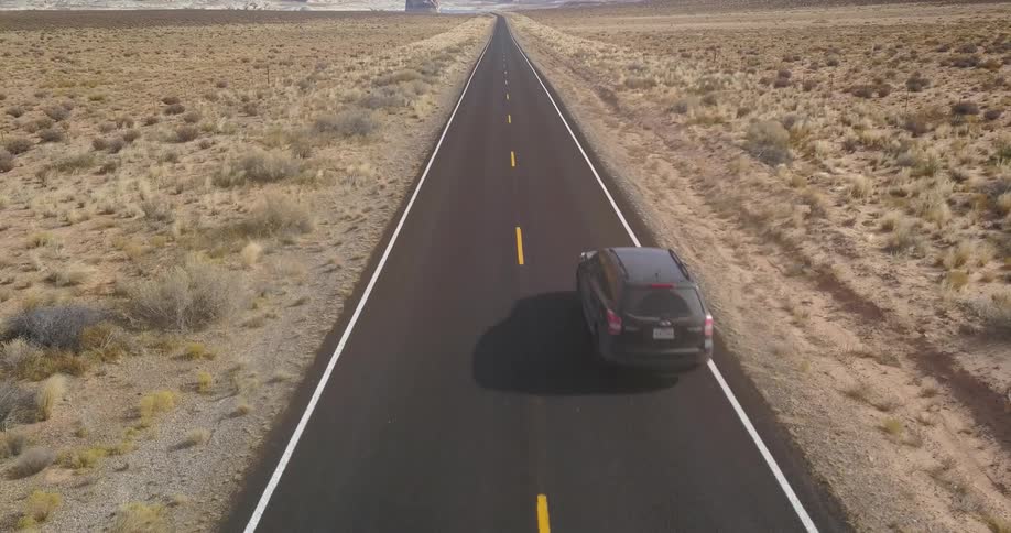A vehicle is traveling over a two-lane desert road during the day