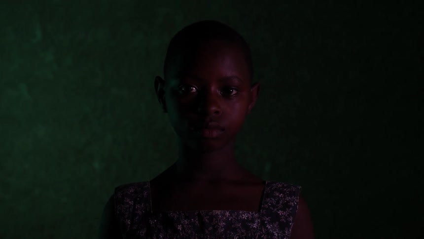 A little girl is standing in front of a wall and staring