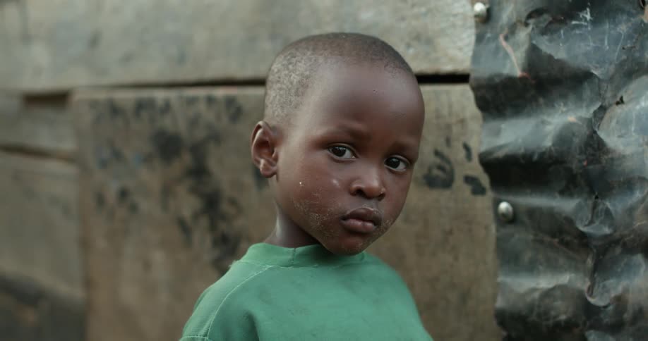 A little boy with a dirty face stands near a wall