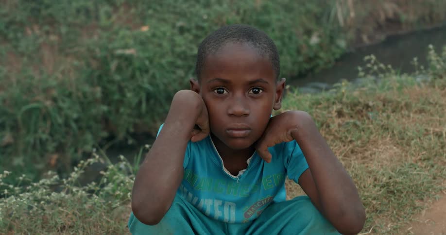 An african child sits and stares as dust drifts past him