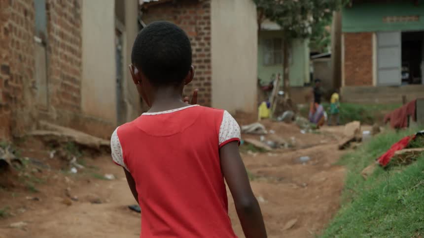 A child walks on a dirt path past houses