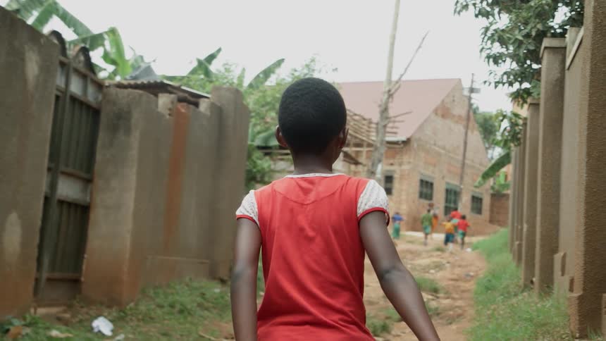 Young children walk down a dirt alley by a school