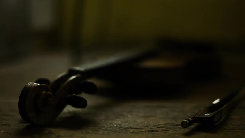 A violin and bow laying on a wooden table shown in closeup