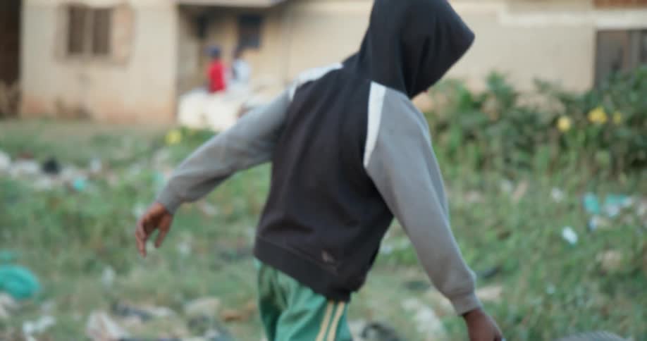 A boy is rolling an old tire around a neighborhood as he plays