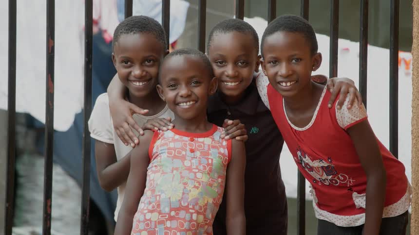 A group of african children stand by a fence smiling and posing