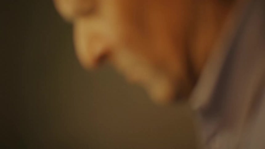 An unfocused headshot of an elderly man looking down while appearing to be talking